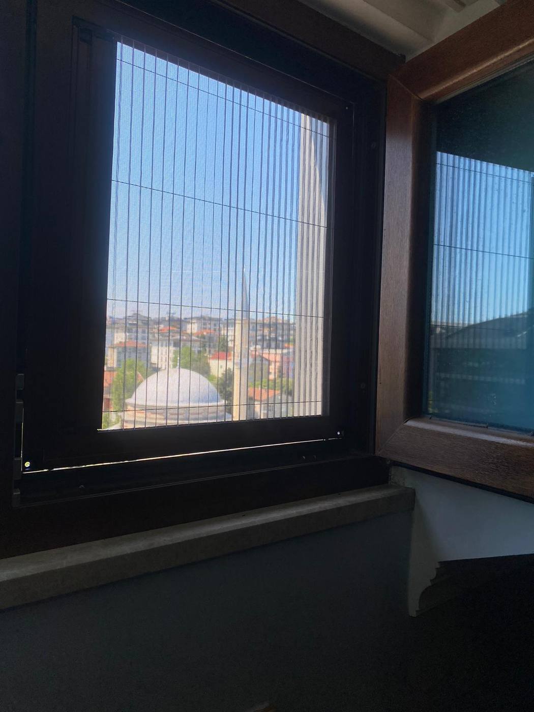 Cami ve şehir manzarasına bakan pencerede sürgülü sineklik